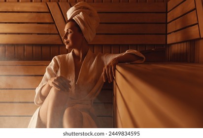 Young woman relaxing and sweating in hot sauna wrapped in towel. Girl In Sauna. Interior of Finnish sauna, classic wooden steam room with hot steam. Russian bathroom. Relax in hot Bathhouse with steam - Powered by Shutterstock