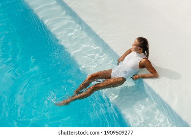 Young woman relaxing in swimming pool on summer vacation. Blonde caucasian model in white bikini floating in water.