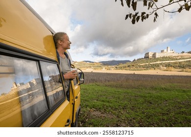 Young woman relaxing in vintage camper van near Assisi hilltop town in Umbria, Italy. Basilica of St. Francis reflection in the window. - Powered by Shutterstock