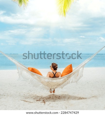 Young woman relaxing in wicker hammock on the sandy beach on Mauritius coast and enjoying wide ocean view waves. Exotic countries vacation and mental health concept image.