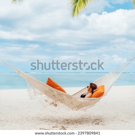 Young woman relaxing in wicker hammock on the sandy white beach on Mauritius coast and enjoying wide ocean view waves. Exotic countries vacation and mental health concept image.
