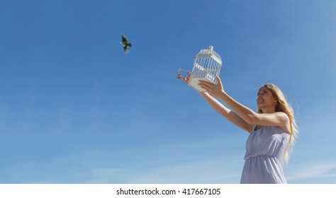 Young woman releasing bird from cage toward blue sky