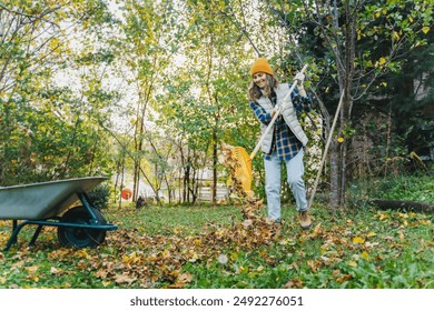 A young woman removes fallen autumn leaves with a rake in the garden of a country house. - Powered by Shutterstock