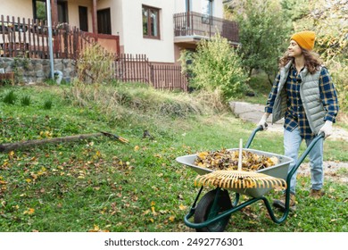 A young woman removes fallen autumn leaves with a rake in the garden of a country house. - Powered by Shutterstock