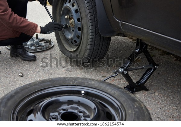 A young woman removes the\
wheel with a key near her car with a flat tire, trouble on the\
road.