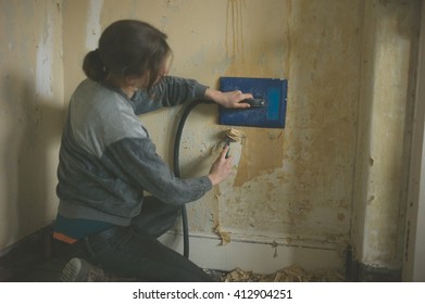 A Young Woman Is Removing Wallpaper With A Steamer