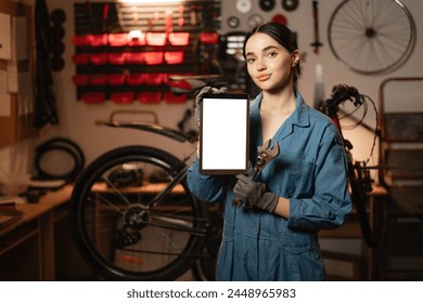 Young woman repairing bicycle in workshop, holding digital tablet with Mockup image. Copy space - Powered by Shutterstock