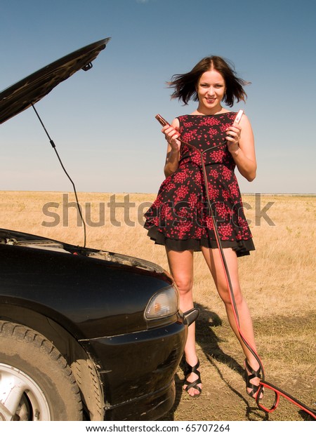 Young\
woman repairing car, connects cleats to the\
battery