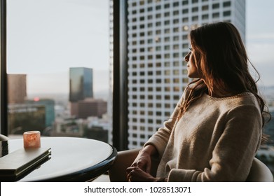 Young woman at restaurant on 35 floor, sitting at table enjoying the city skyline at sunset with stunning panoramic view of Los Angeles.