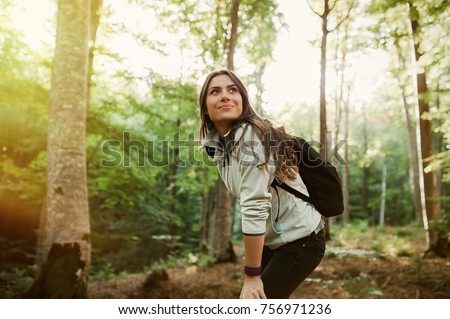 Young woman resting after a walk in the forest, carrying a backpack in the forest on sunset light in the autumn season.