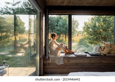 Junge Frau, die sich in einem schönen Landhaus oder Hotel, sitzend auf dem Fenster ruht, genießen einen schönen Blick auf Kiefernwald. Konzept der Einsamkeit und Erholung in der Natur