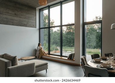 Young woman resting at beautiful country house or hotel, sitting on the window sill enjoying beautiful view on pine forest. Concept of solitude and recreation on nature rest  - Powered by Shutterstock