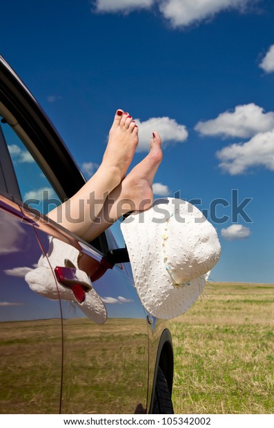 Young woman\
resting in car with legs out of\
window.