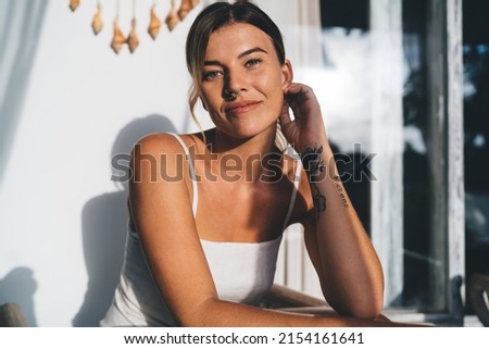 Young woman resting and looking at camera on terrace of resort hotel. Concept of tourism, vacation and weekend. Beautiful caucasian girl. Sunny day. Idyllic and tranquil lifestyle on Bali island