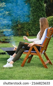 Young Woman Resting In Lounge Chair On Backyard Next To A Barbecue, View On Profile