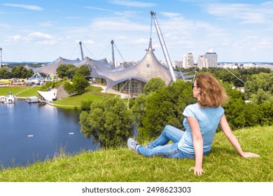 Young woman rests in Olympic park in summer, Munich, Germany. This place is famous landmark of Munchen city. Concept of travel people, tourism, sport and sightseeing in Munich. - Powered by Shutterstock