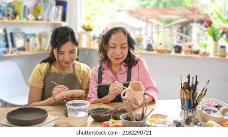 Young woman and retired woman painting painting on bowl before baking in pottery workshop - Powered by Shutterstock