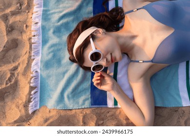 Young woman in retro glasses and blue swimsuit lying on the beach striped towel. Summer vacation fashion and beauty lifestyle concept - Powered by Shutterstock