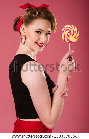Young woman in retro style posing with a lollypop candy on the pink background. Pinup portrait