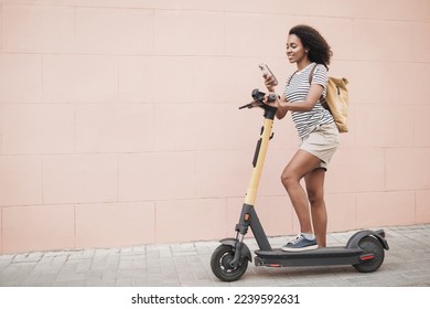 Young woman rides on electric scooter and using smartphone in a city. Smiling girl looking at mobile phone on a street - Powered by Shutterstock