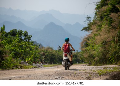 Young woman rides the scooter on an empty road in tropics with mountains on the background - Powered by Shutterstock