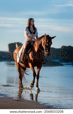 Young woman riding a chestnut horse in a beach
