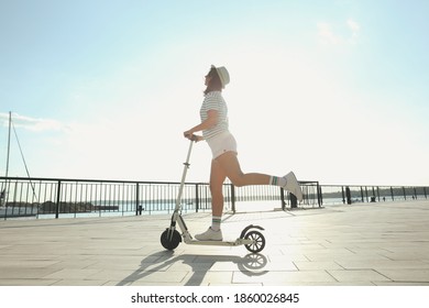 Young Woman Riding Modern Kick Scooter Along Waterfront