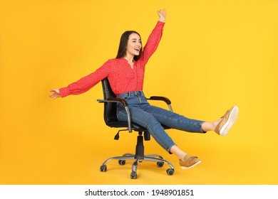 Young Woman Riding Office Chair On Yellow Background