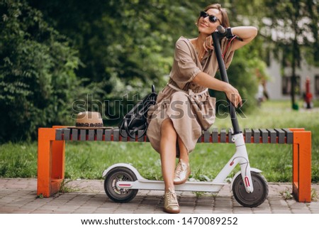 Young woman riding scooter in park sitting on bench