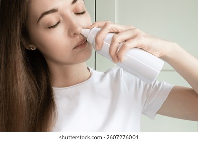 Mujer joven que se enjuaga la nariz con la botella del aerosol de la solución salina para aliviar la congestión, las alergias estacionales, la nariz mocosa. 