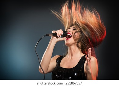 A young woman rock singer with tousled long hair holding a microphone with stand and sing with a wide open mouth. - Powered by Shutterstock