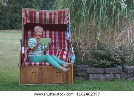 The young woman in the roofed wicker beach chair is happy about the great shopping on the Internet