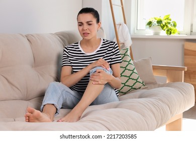 Young Woman Rubbing Sore Leg On Sofa At Home