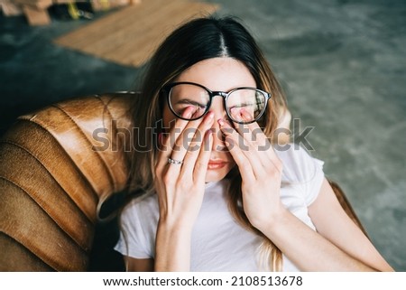 Young woman rubs her eyes after using glasses. Eye pain or fatigue concept.