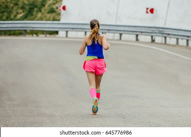 Young Woman Runner In Bright Pink Compression Socks Running On Mountain Road