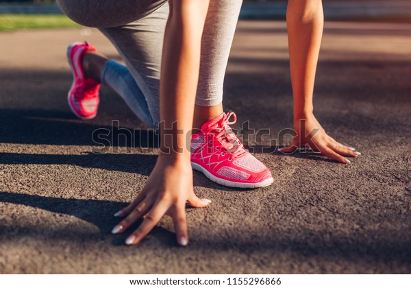 Young woman runner getting off to an early\
start on sportsground in summer. Close up of sneakers and hands.\
Active lifestyle