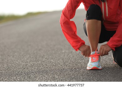 young woman runner tying shoelace on country road - Powered by Shutterstock