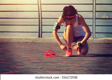 Young Woman Runner Tying Shoelace At Seaside