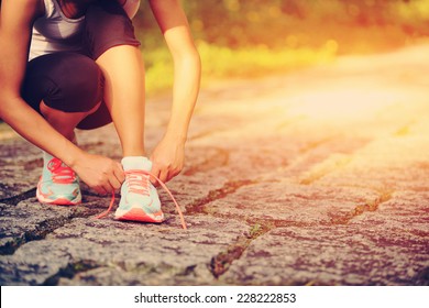 young woman runner tying shoelaces on country road 