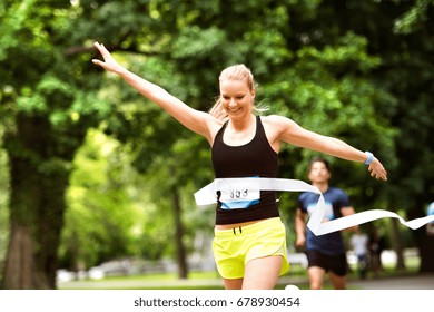 Young Woman Running In The Crowd Crossing The Finish Line.