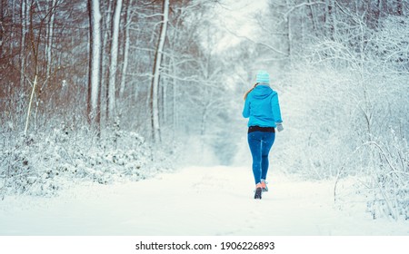 Young Woman Running Down A Path In The Winter Woods Through Snow Away From Camera