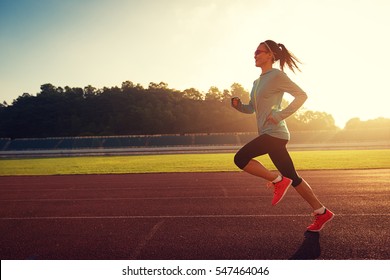 Young woman running during sunny morning on stadium track - Powered by Shutterstock