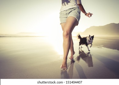 Young Woman Running With Her Dog In The Shallow Water On The Beach.