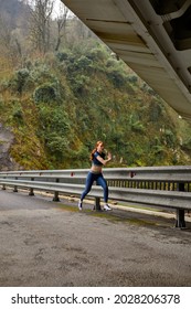 Young Woman Running Jogging Fast Outdoors. Female Athlete Exercising On Modern Bridge. Side View On Strong Active Vigorous Lady In Blue Sportswear Running Forward, Copy Space. Sport Concept