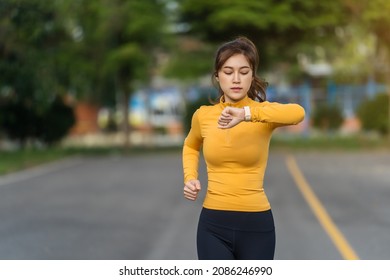 Young Woman Running And Looking At Her Smart Wrist Watch In The Park