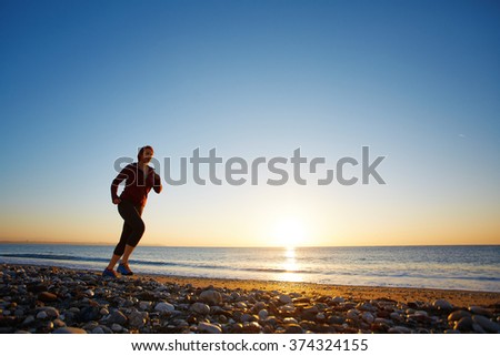 young woman running on the beach against sea and blue sky at the sunrise