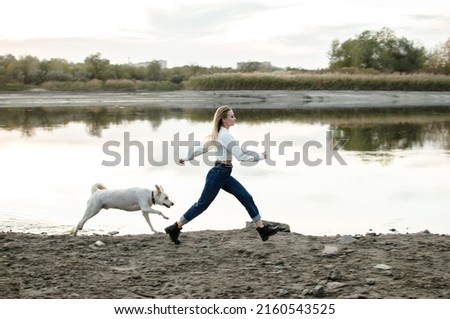 A young woman runs walking her dog along the riverbank outdoors.