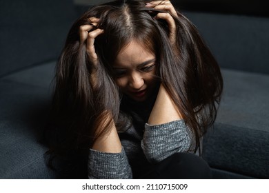 Young woman sad, sitting, catch head, bow head, depression emotion on face, looking down in dark room, Portrait of young beautiful woman or female or girl sitting expression depression emotional alone