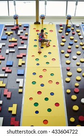 Young Woman In Safety Harness Has Almost Reached The Top Of The Climbing Wall In Indoor Rock-climbing Center