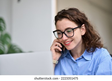 Young woman sales manager talking on cell phone using laptop working online on computer. Female professional entrepreneur making call consulting customer on mobile selling e services in office. - Shutterstock ID 2223351475